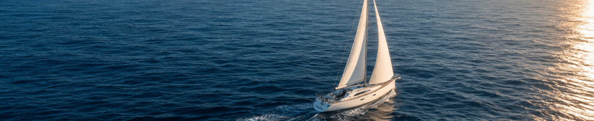 White sailboat navigating across deep blue ocean water toward warm sunlight, representing guidance, direction, and compliance readiness.